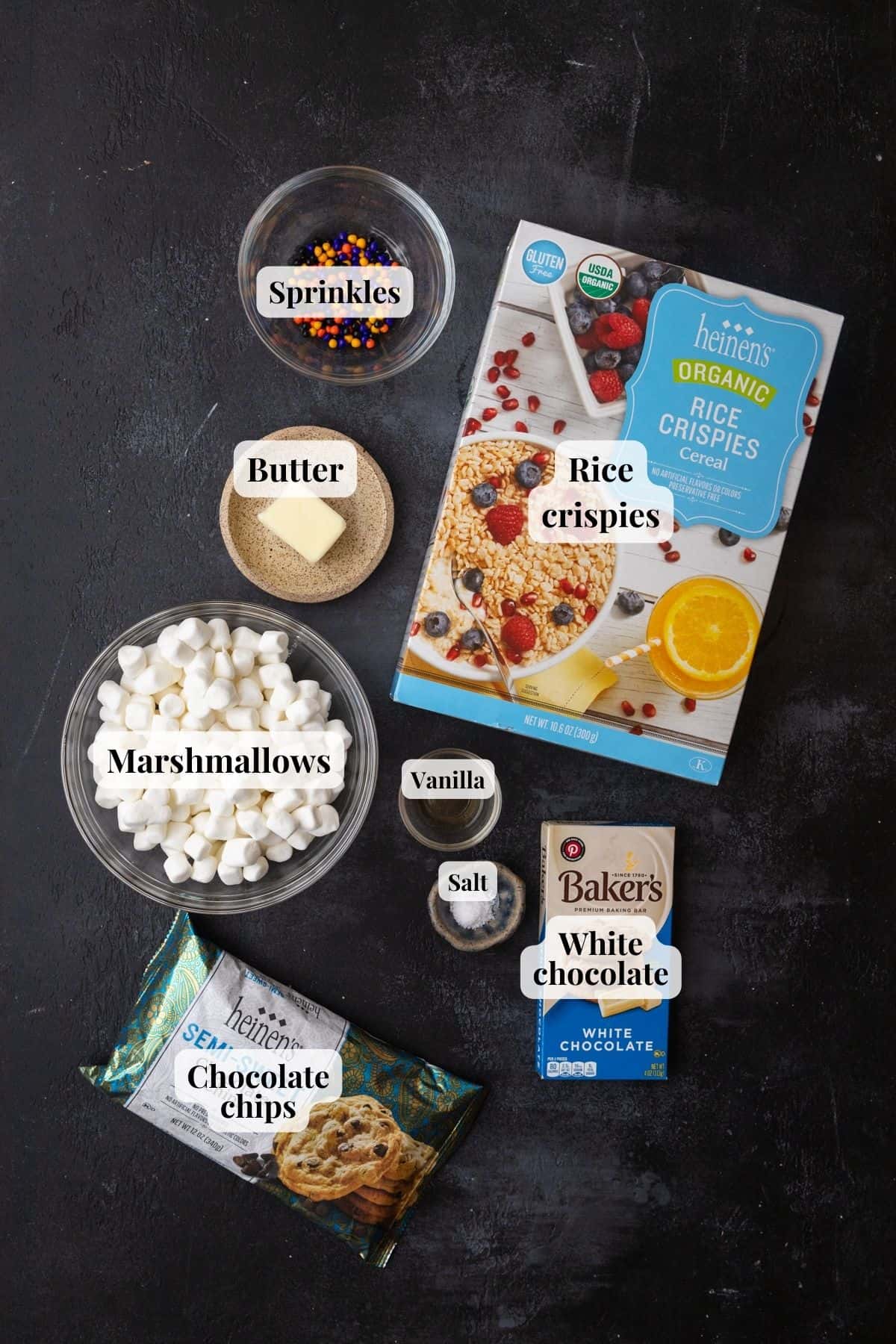 Ingredients to make chocolate dipped Rice Krispie treats on a black surface.