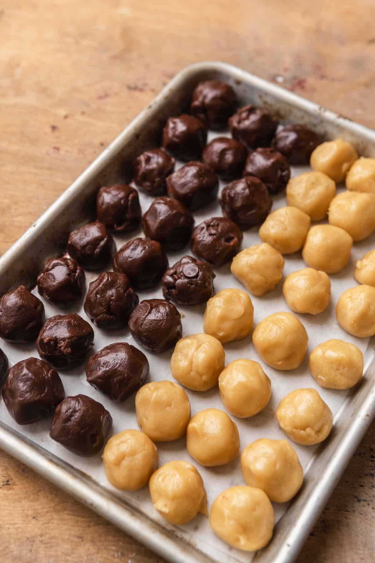 Plain and chocolate cookie dough balls on a cookie sheet.