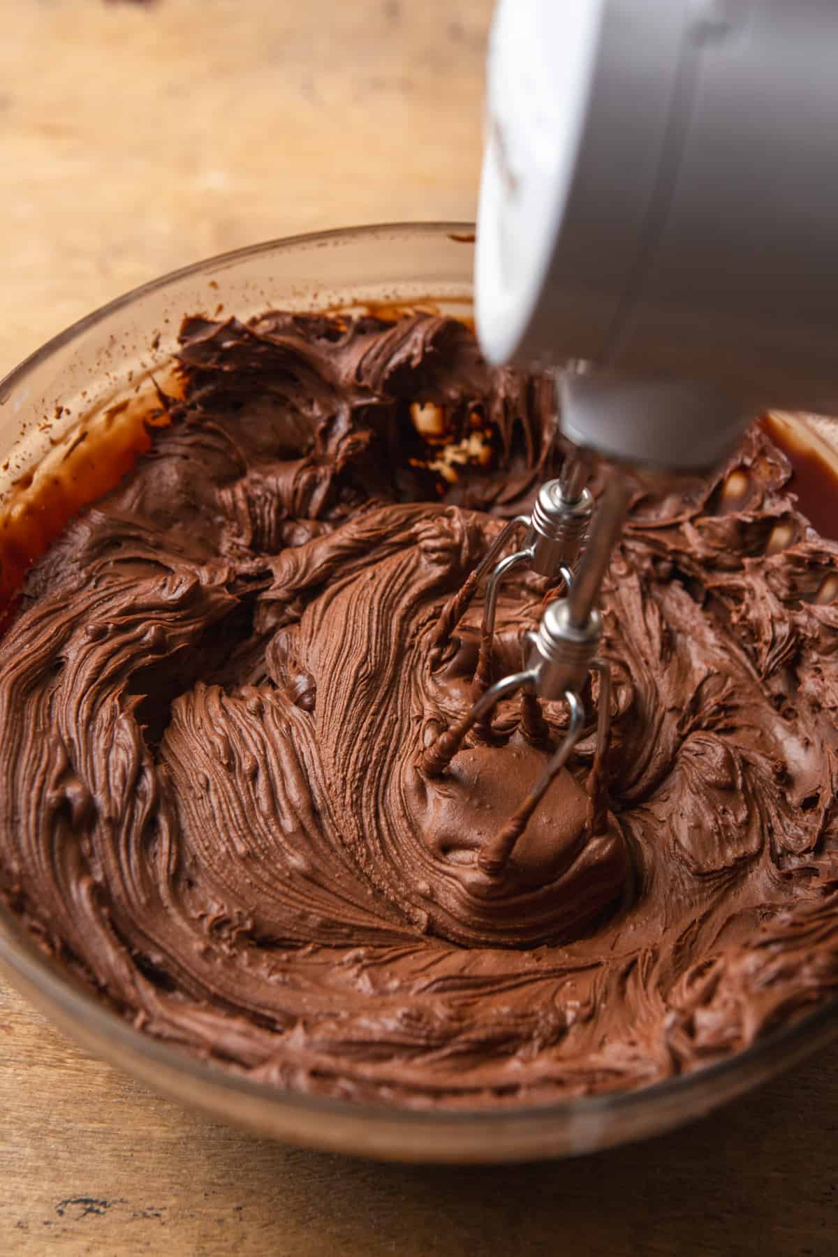Mixing ganache with a hand mixer in a glass bowl.