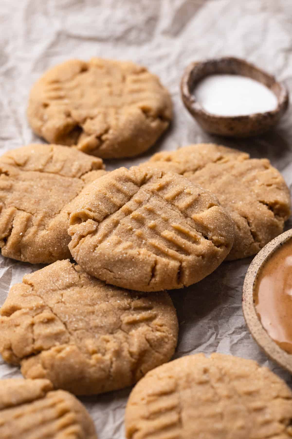Cookies laying on crinkled parchment paper with bowls of sugar and peanut butter.