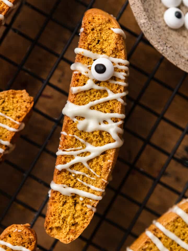 Halloween pumpkin biscotti on a cooling rack with candy eyes.