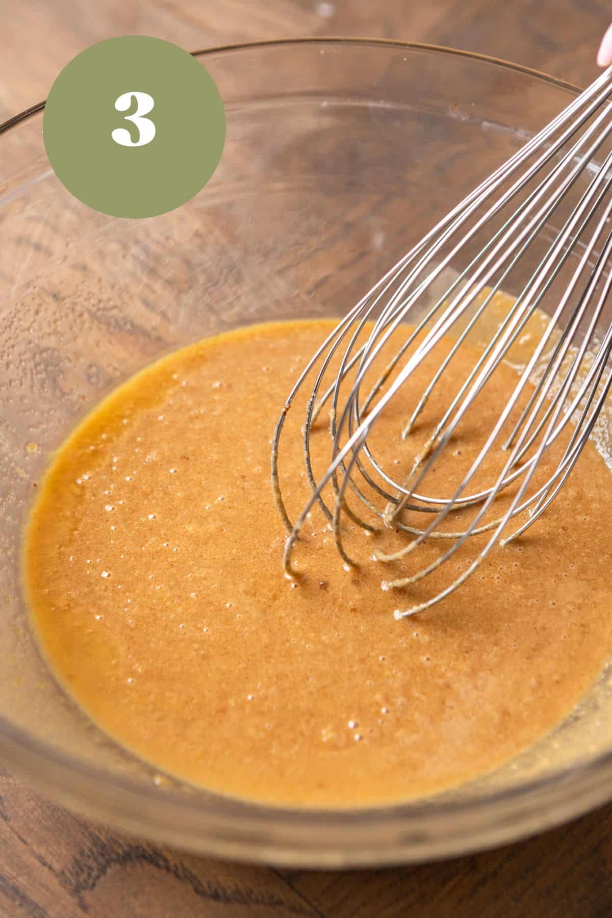 Melted butter, sugar, and peanut butter being whisked together in a glass bowl.
