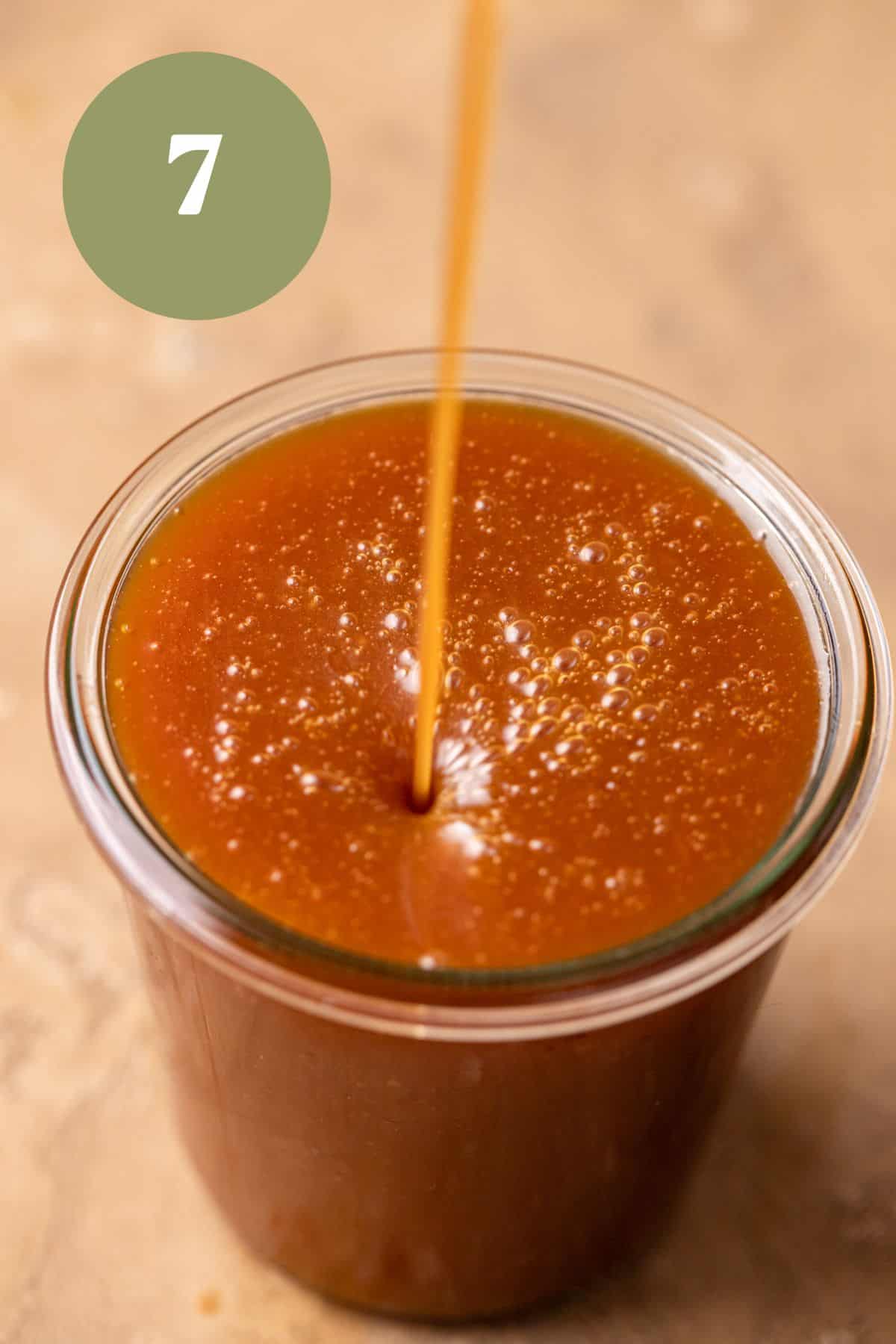 Pouring caramel sauce into a glass jar.