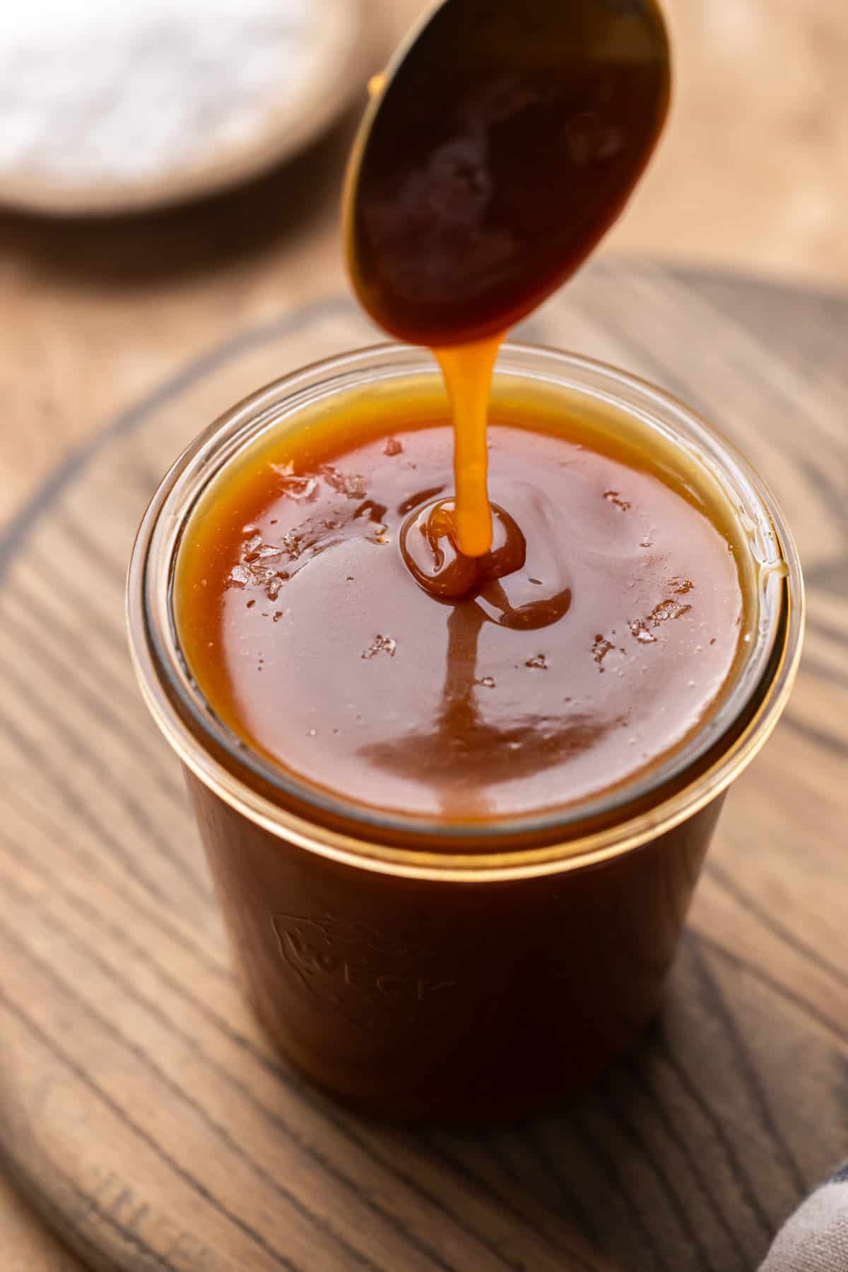 Drizzling salted caramel into a jar with a spoon.