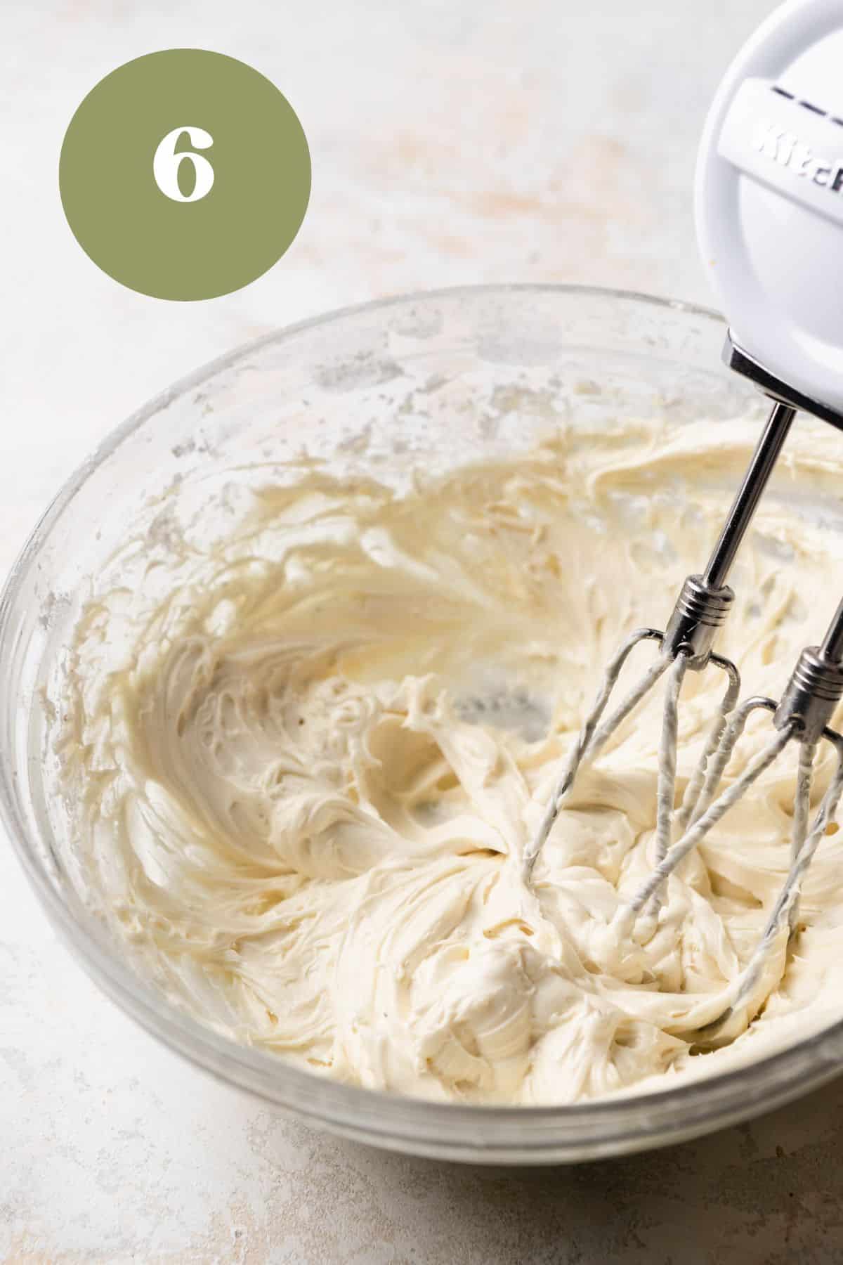 Beating cream cheese frosting in a bowl with a hand mixer.