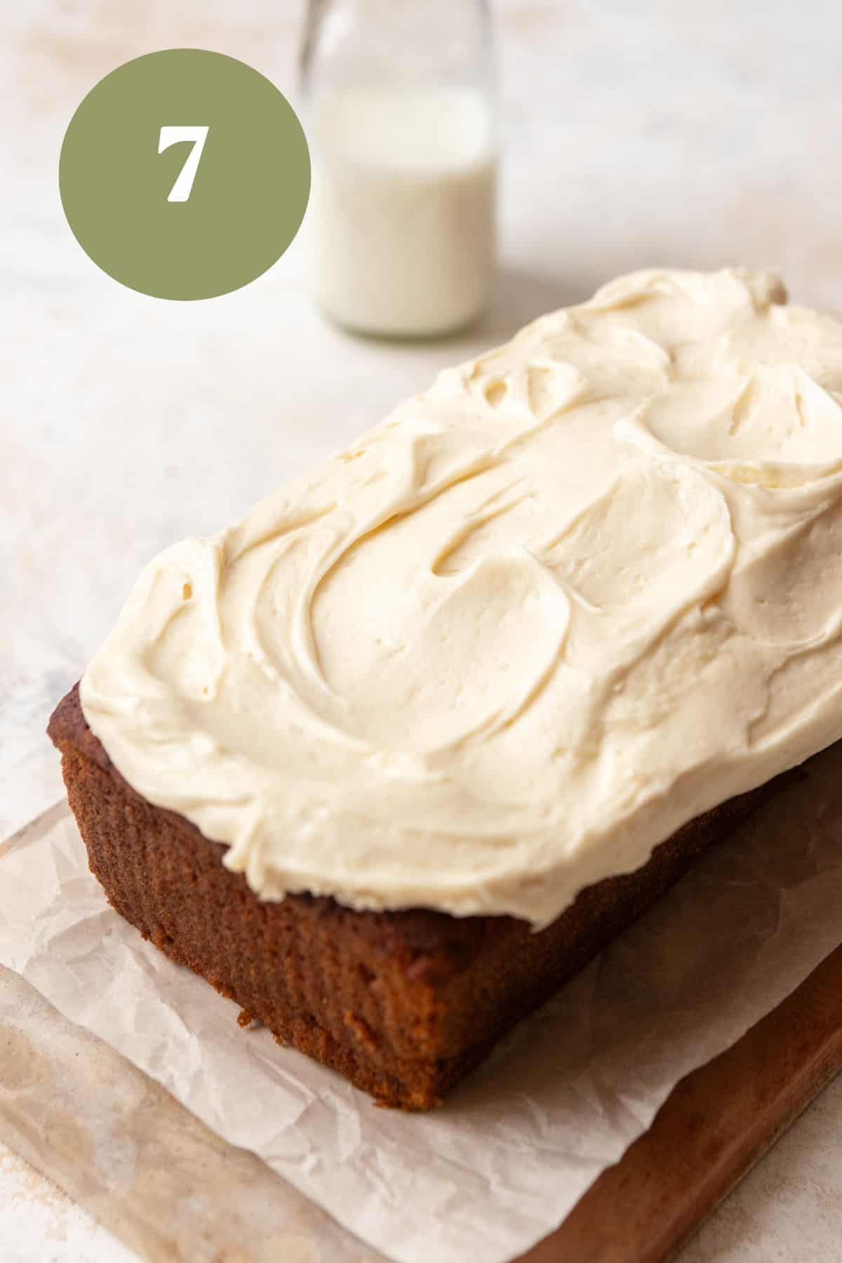 Banana bread with cream cheese frosting on a wood board.