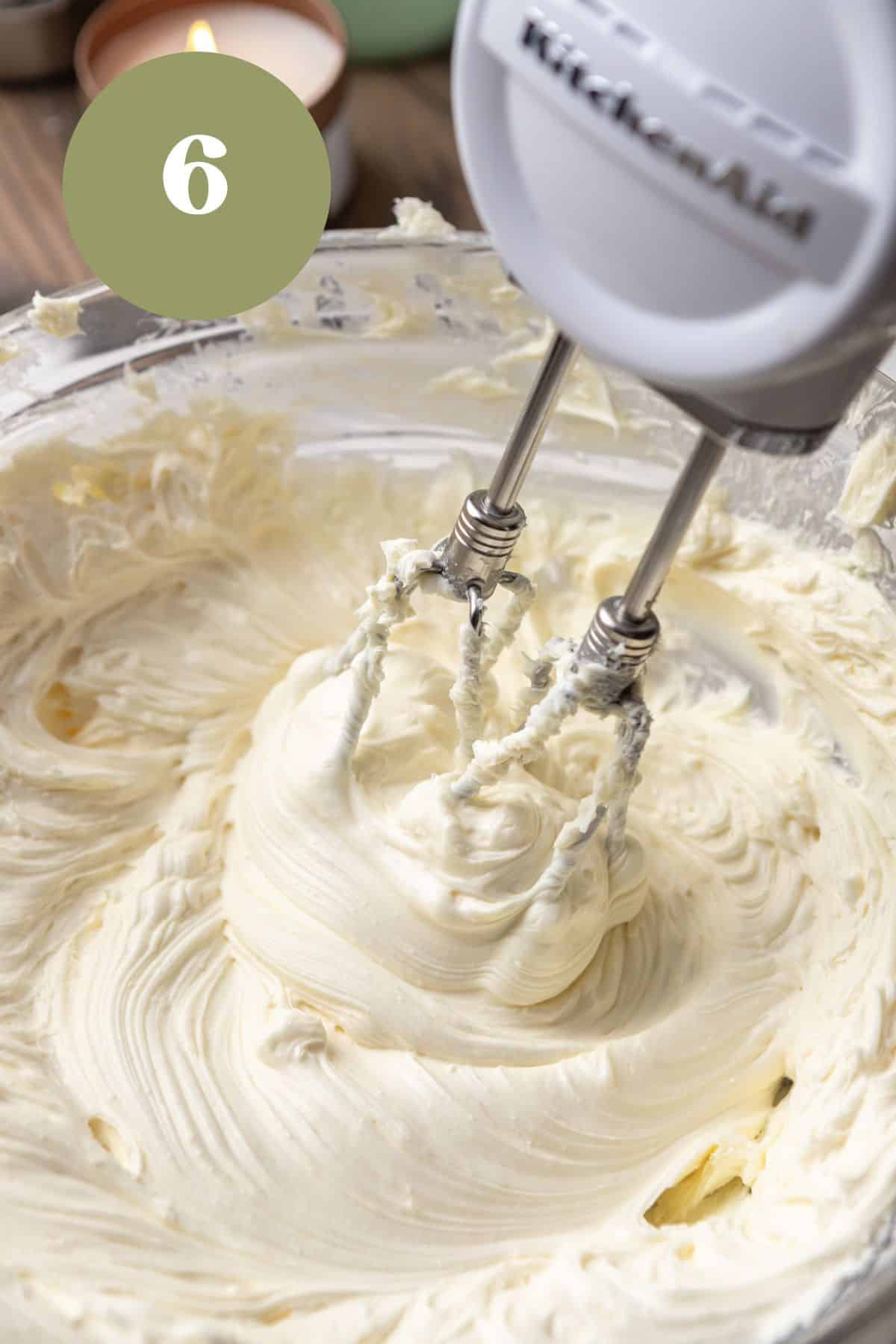 A hand mixer mixing cream cheese and sugar together in a bowl.
