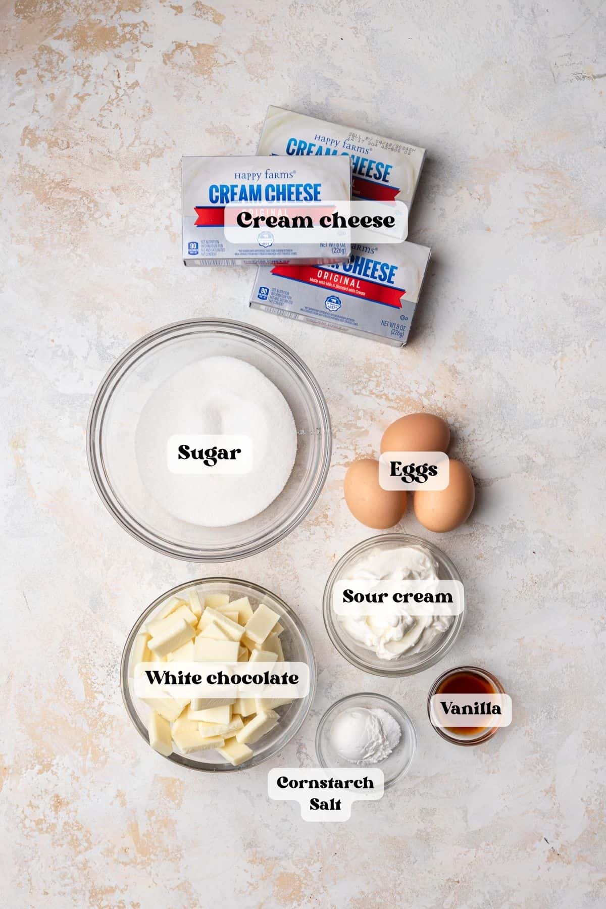 Ingredients to make white chocolate Oreo cheesecake on a white surface.