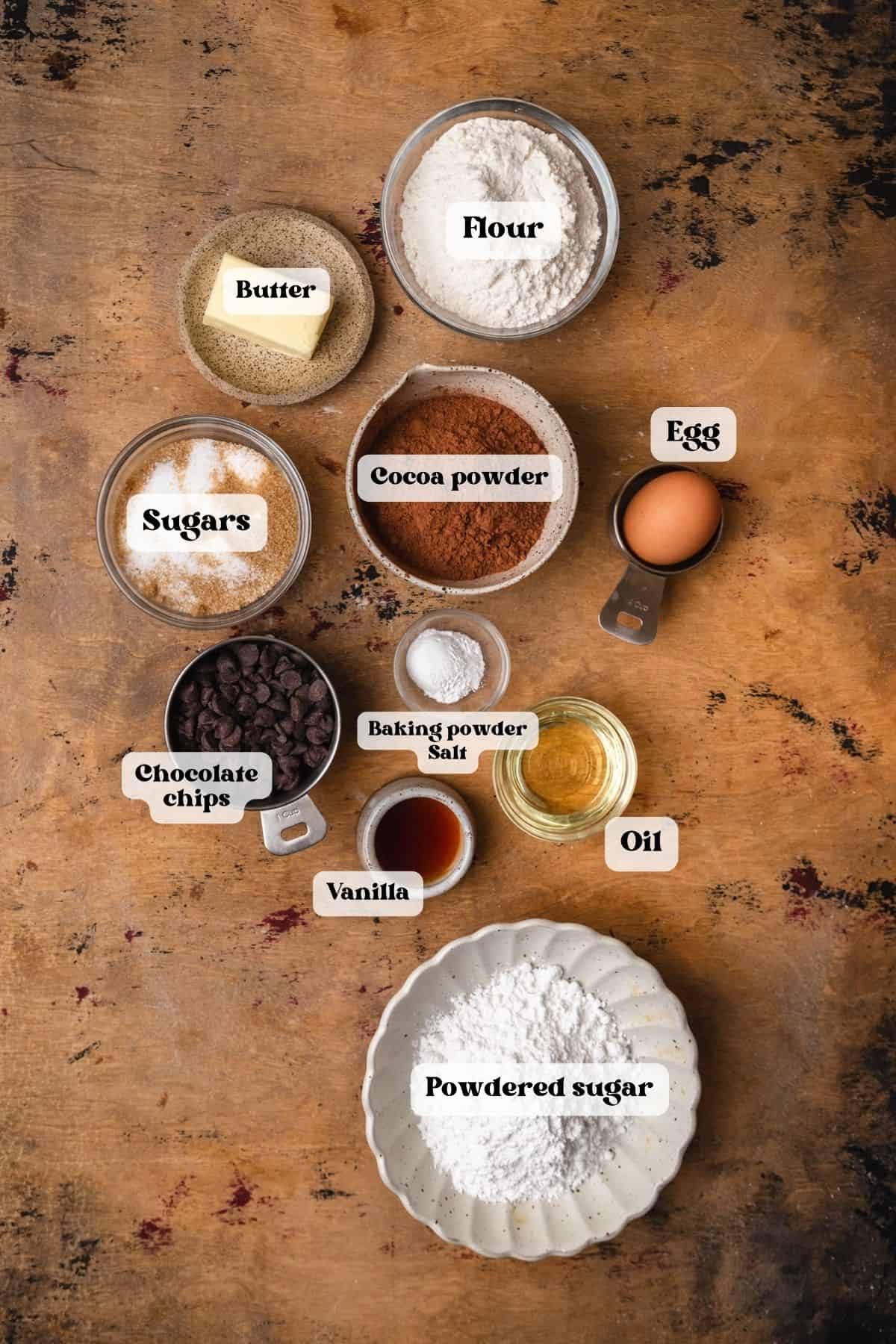 Ingredients to make chocolate snowstorm cookies on a wood surface.