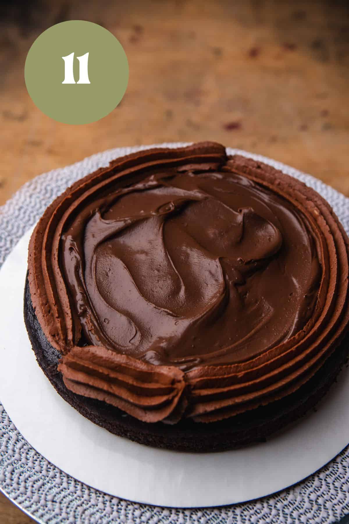 A cake layer with frosting a chocolate ganache on a cake board.