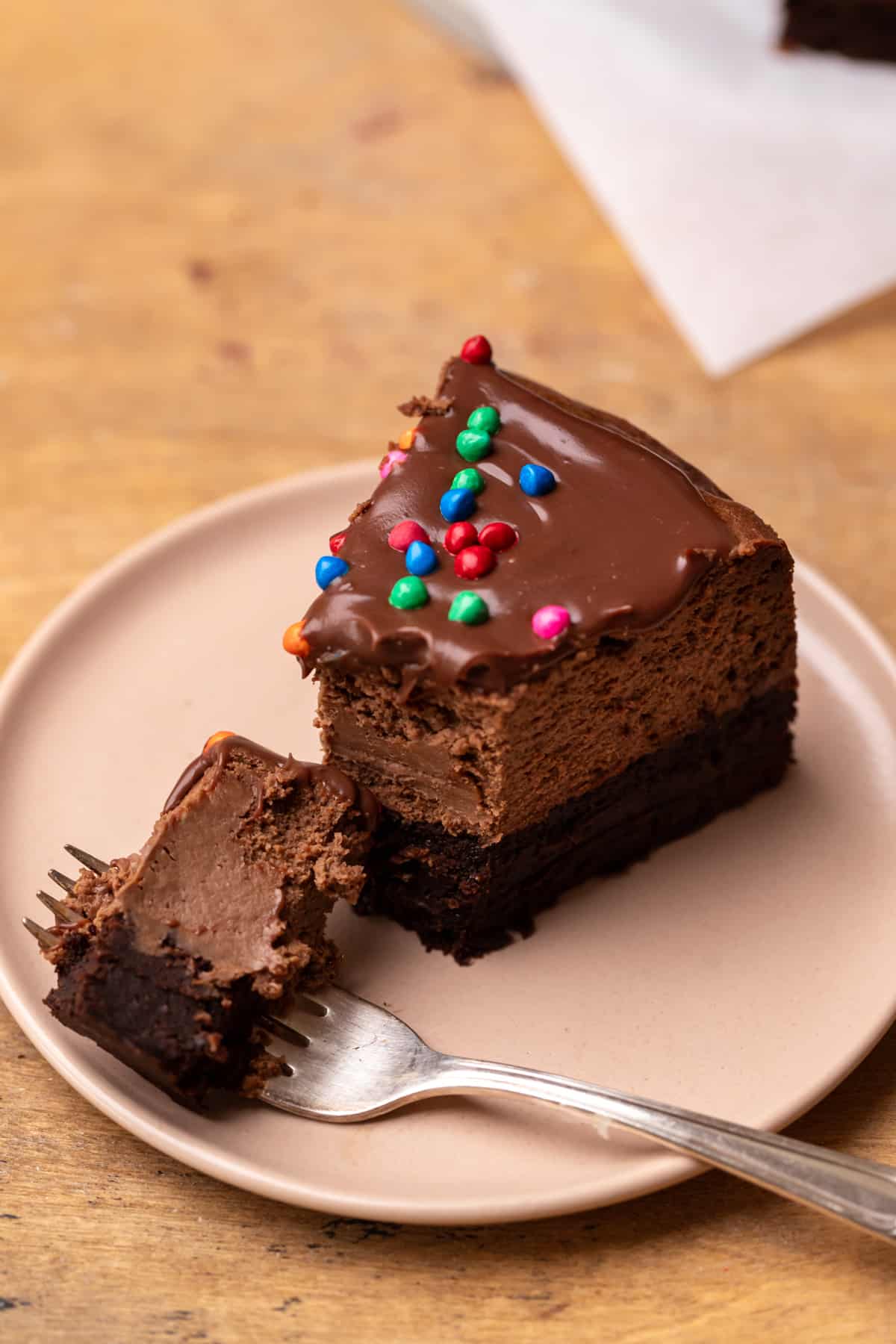 A slice of cosmic brownie cheesecake on a pink plate with a fork that has cut into it.