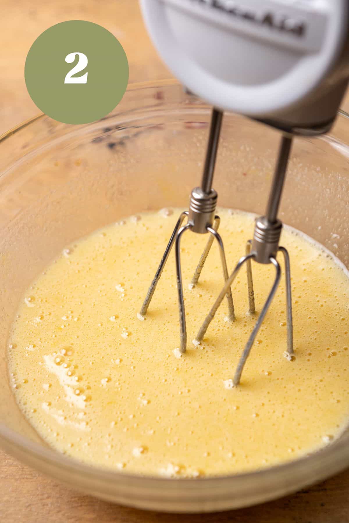 Eggs and sugar mixed together in a bowl with an electric mixer.