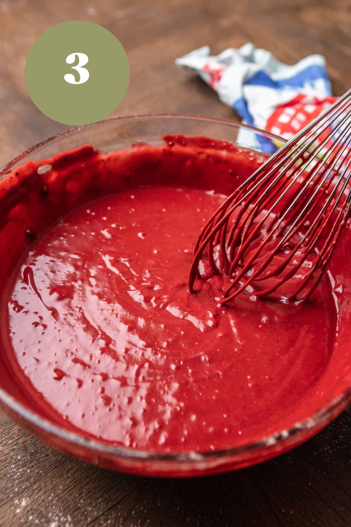 Red velvet cake batter in a bowl with a whisk.