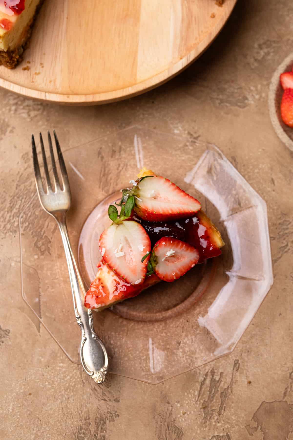 A slice of cheesecake topped with strawberries on a beige surface.