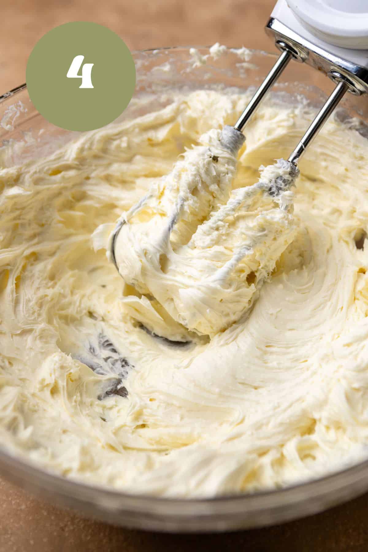 Creamed cream cheese and sugar in a bowl with a hand mixer.