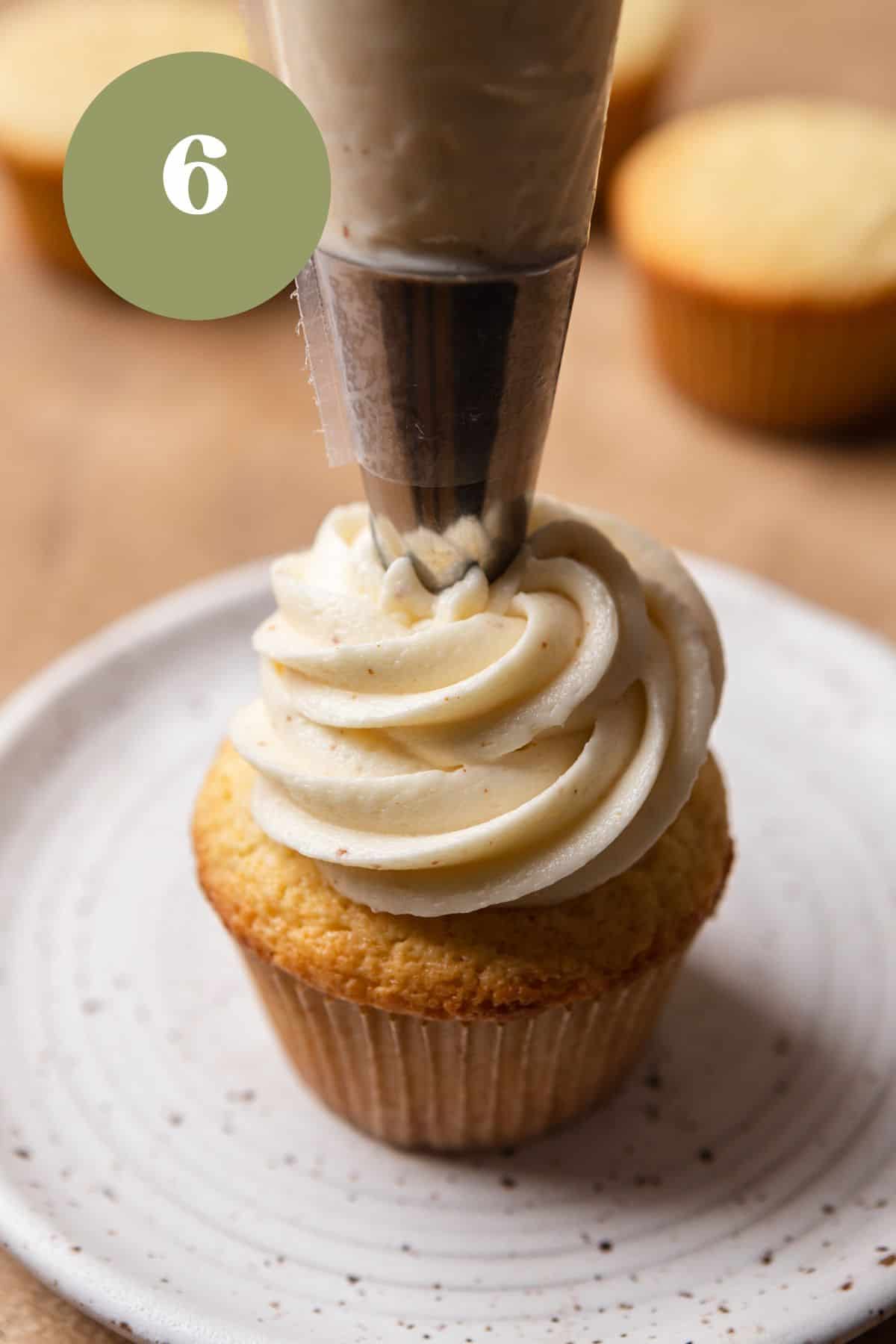 A cupcake on a white plate being piped with frosting.
