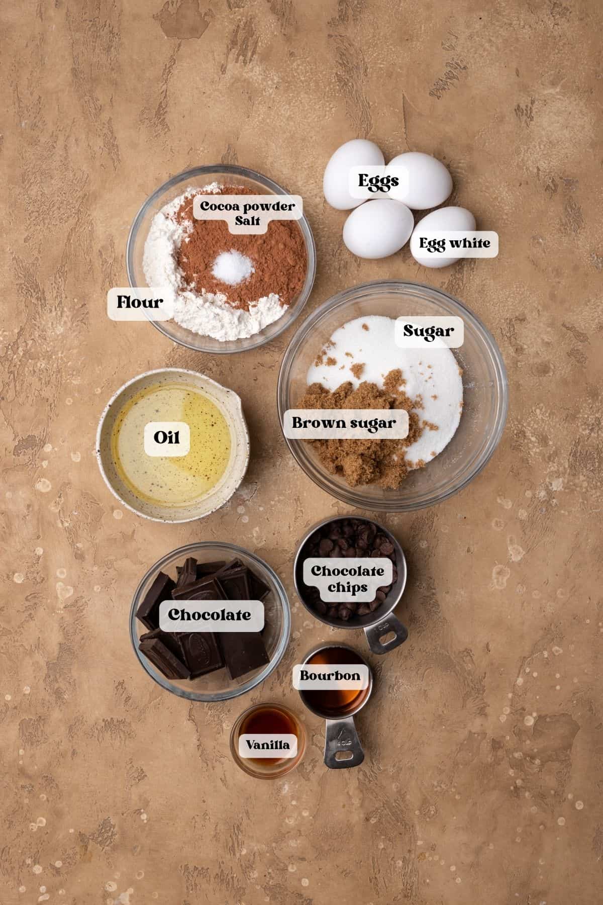 Ingredients to make bourbon fudge brownies on a tan surface.