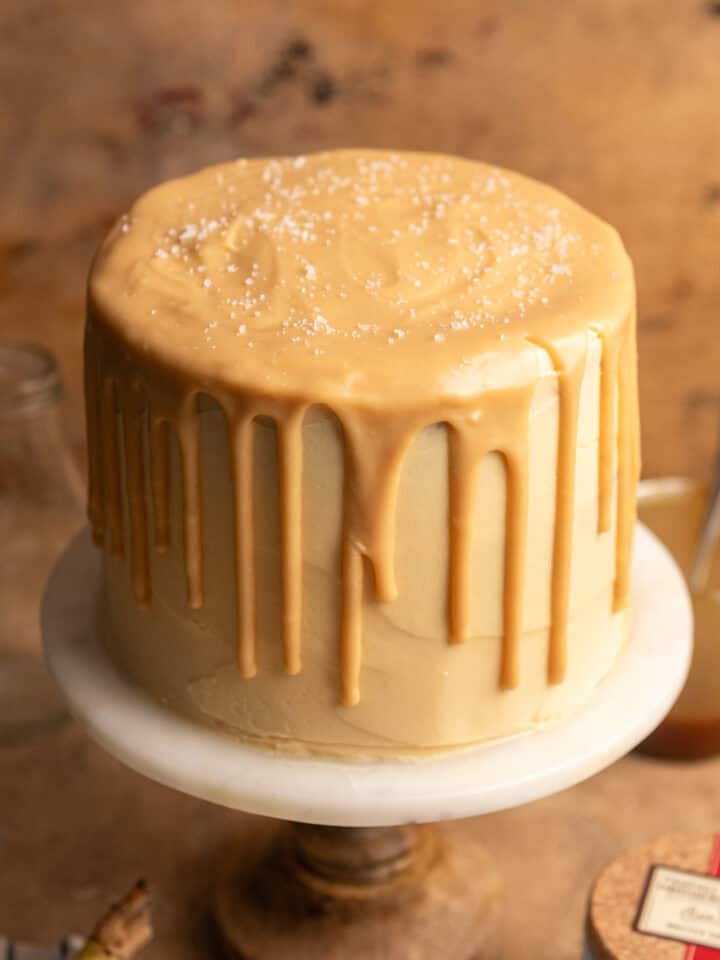 A banana caramel layer cake on a marble cake stand with a caramel ganache drip.