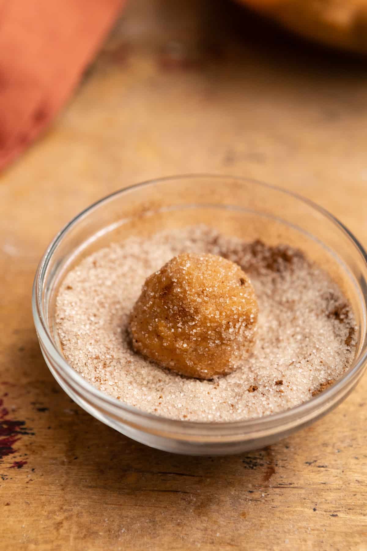 A ball of cookie dough in a small bowl of cinnamon sugar.