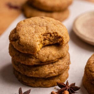 A stack of pumpkin spice cookies on parchment paper with a bite taken out of one.