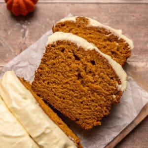 Slices of pumpkin bread with cream cheese frosting on parchment paper.