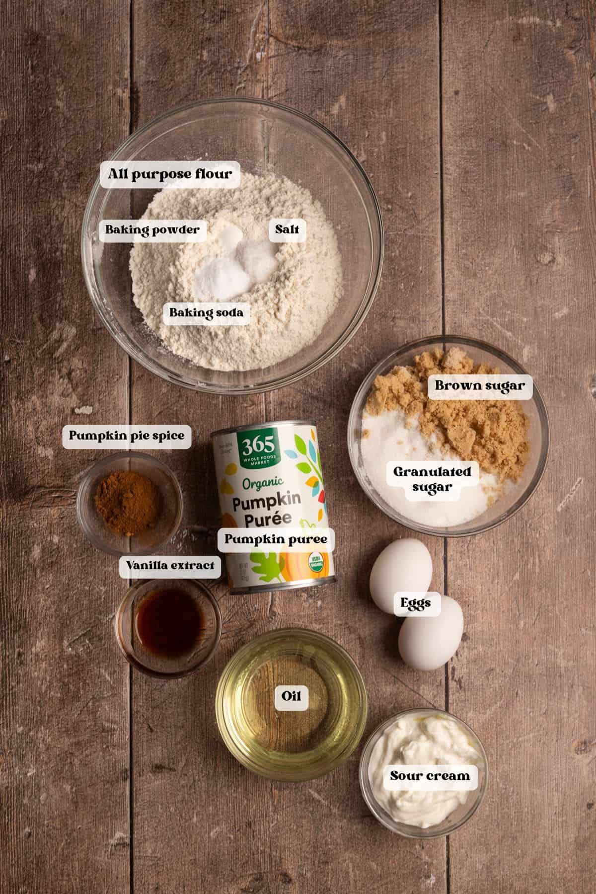 Ingredients for pumpkin bread in bowls on a brown wood surface.