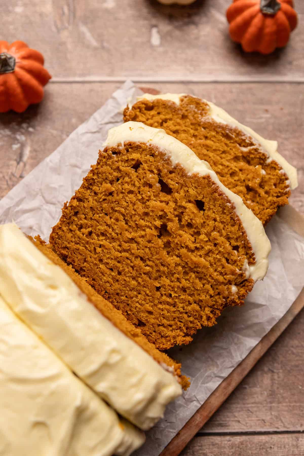 Slices of pumpkin bread frosted with cream cheese frosting on wood surface.