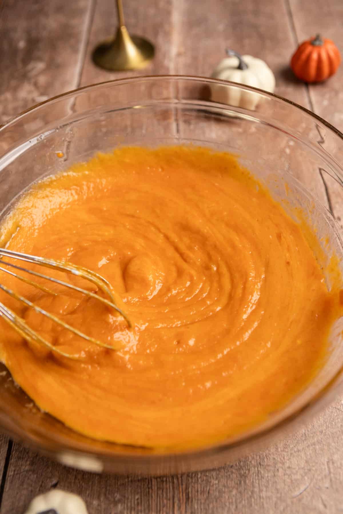 Pumpkin mixed with oil and eggs in a bowl with a whisk.