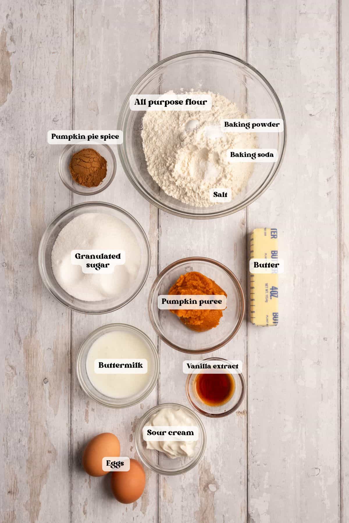 Ingredients to make pumpkin cupcakes on a white wood surface.