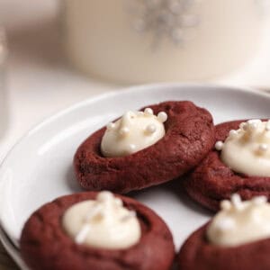 Red velvet thumbprint cookies filled with cream cheese on a white plate.