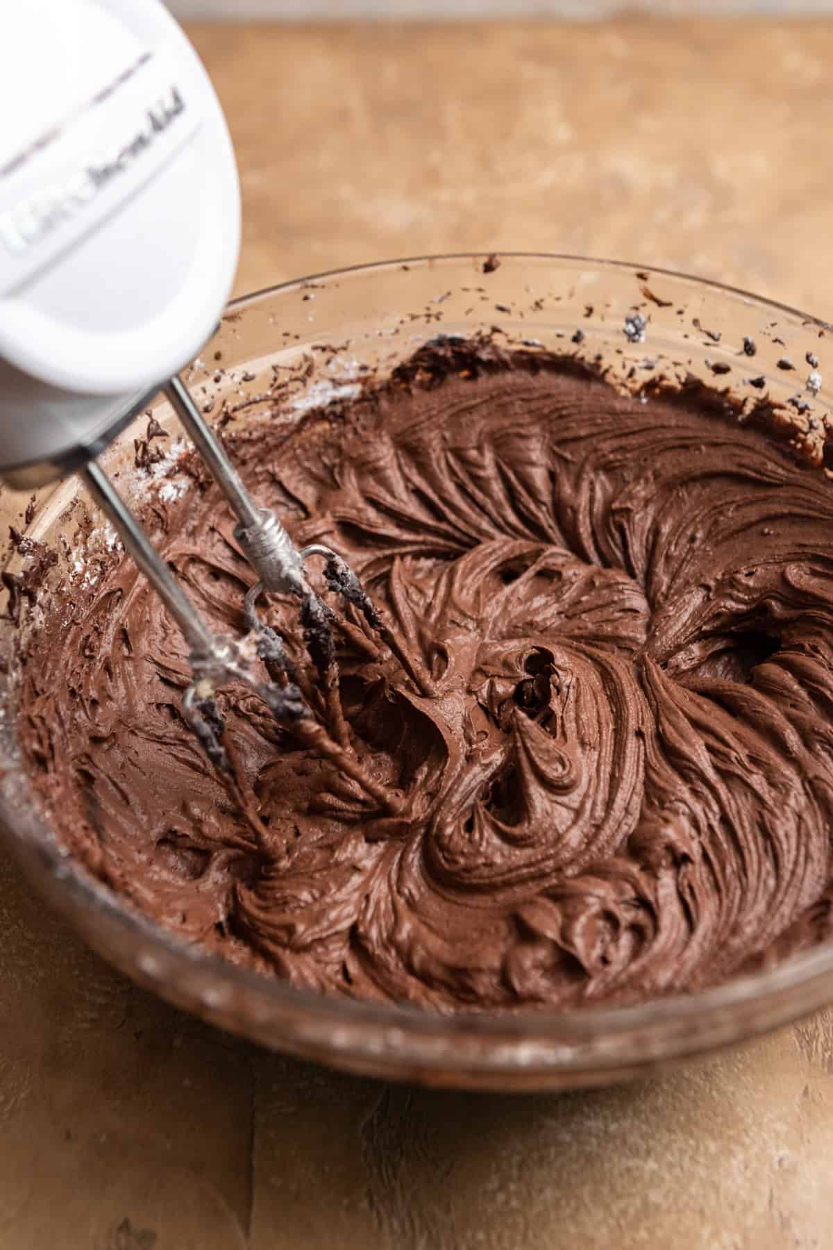 Chocolate buttercream being mixed with an electric mixer.
