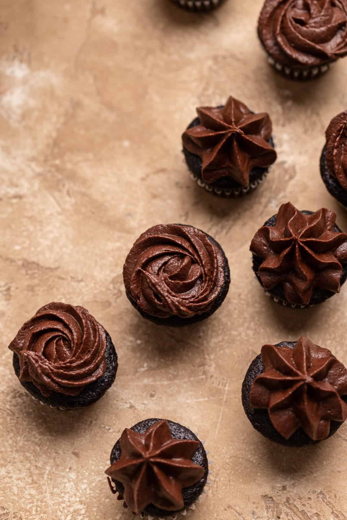 Mini chocolate cupcakes on a beige surface.