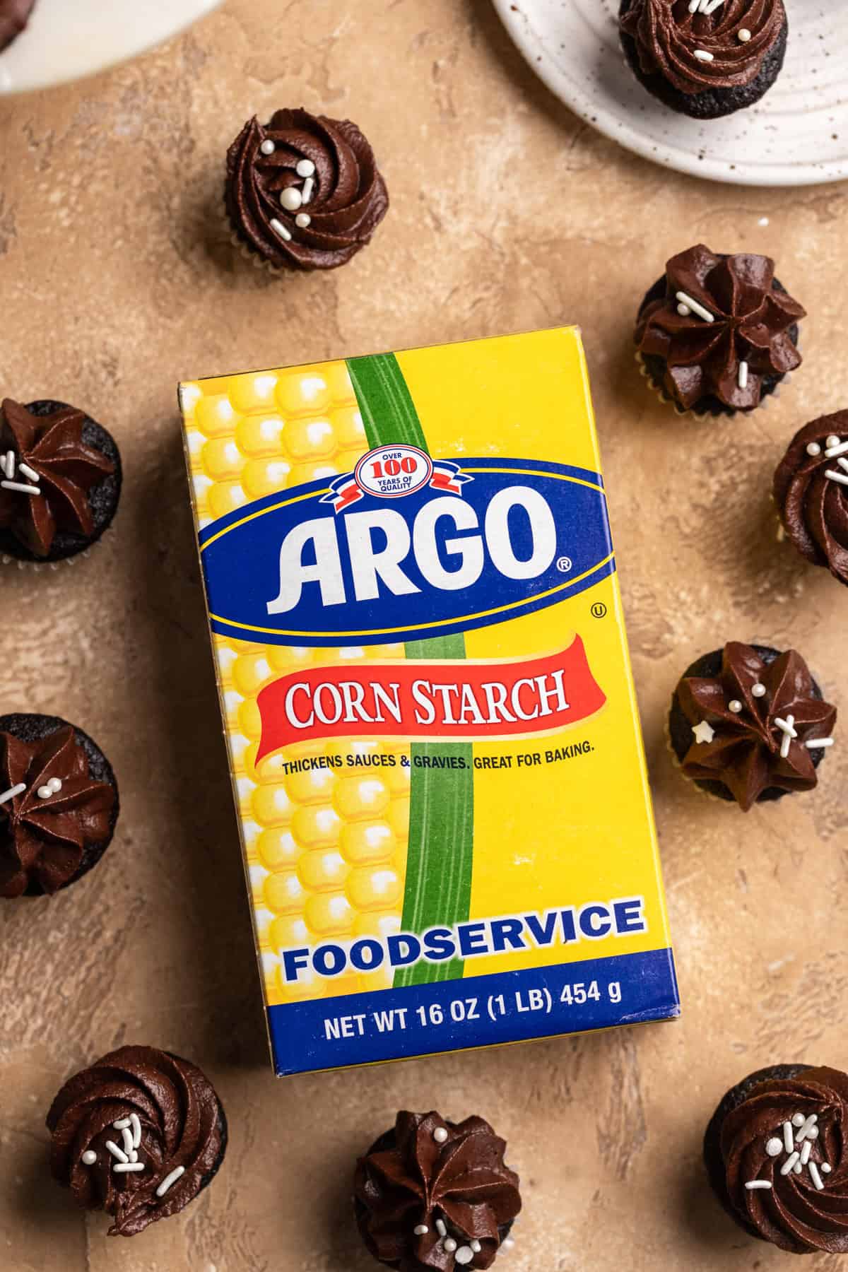 A box of corn starch surrounded by mini chocolate cupcakes.
