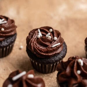 A close up of mini chocolate cupcakes with white sprinkles.