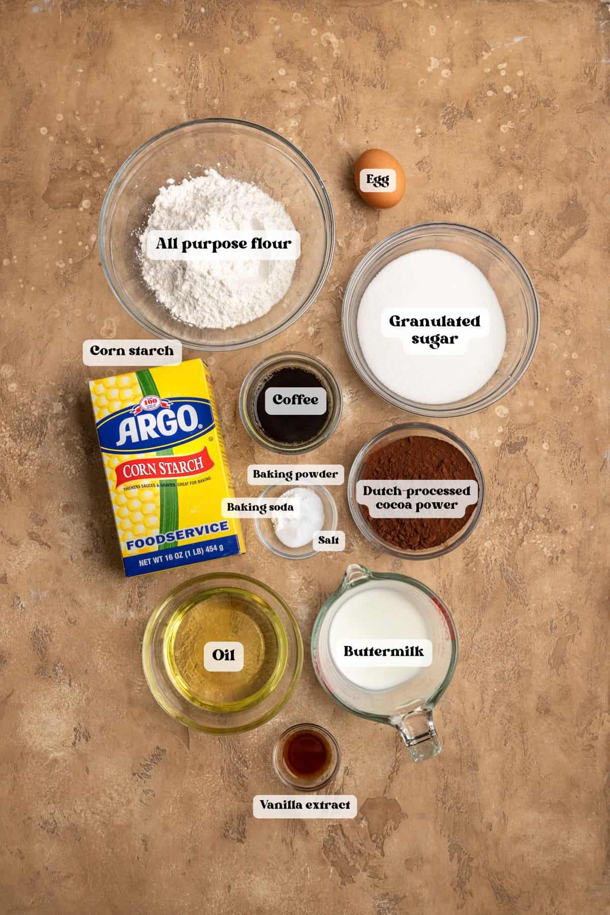 Ingredients to make chocolate cupcakes on a tan surface.