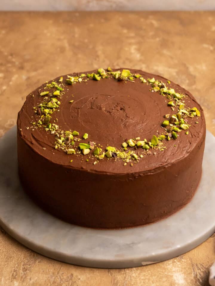 Chocolate pistachio cake with chopped pistachios on top on a marble cake stand.