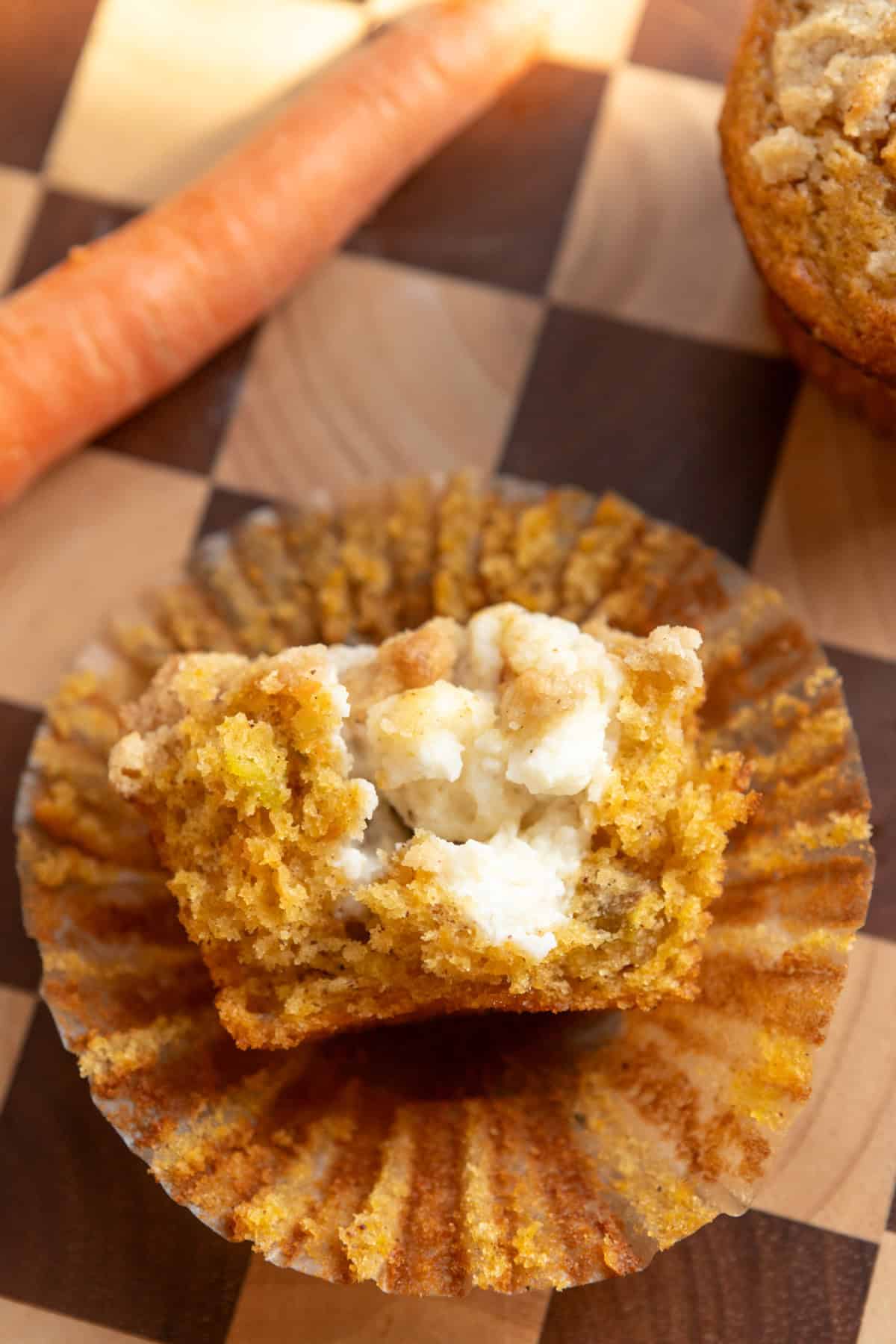 Half of a carrot cake muffin with a cream cheese center on a checkered serving board.