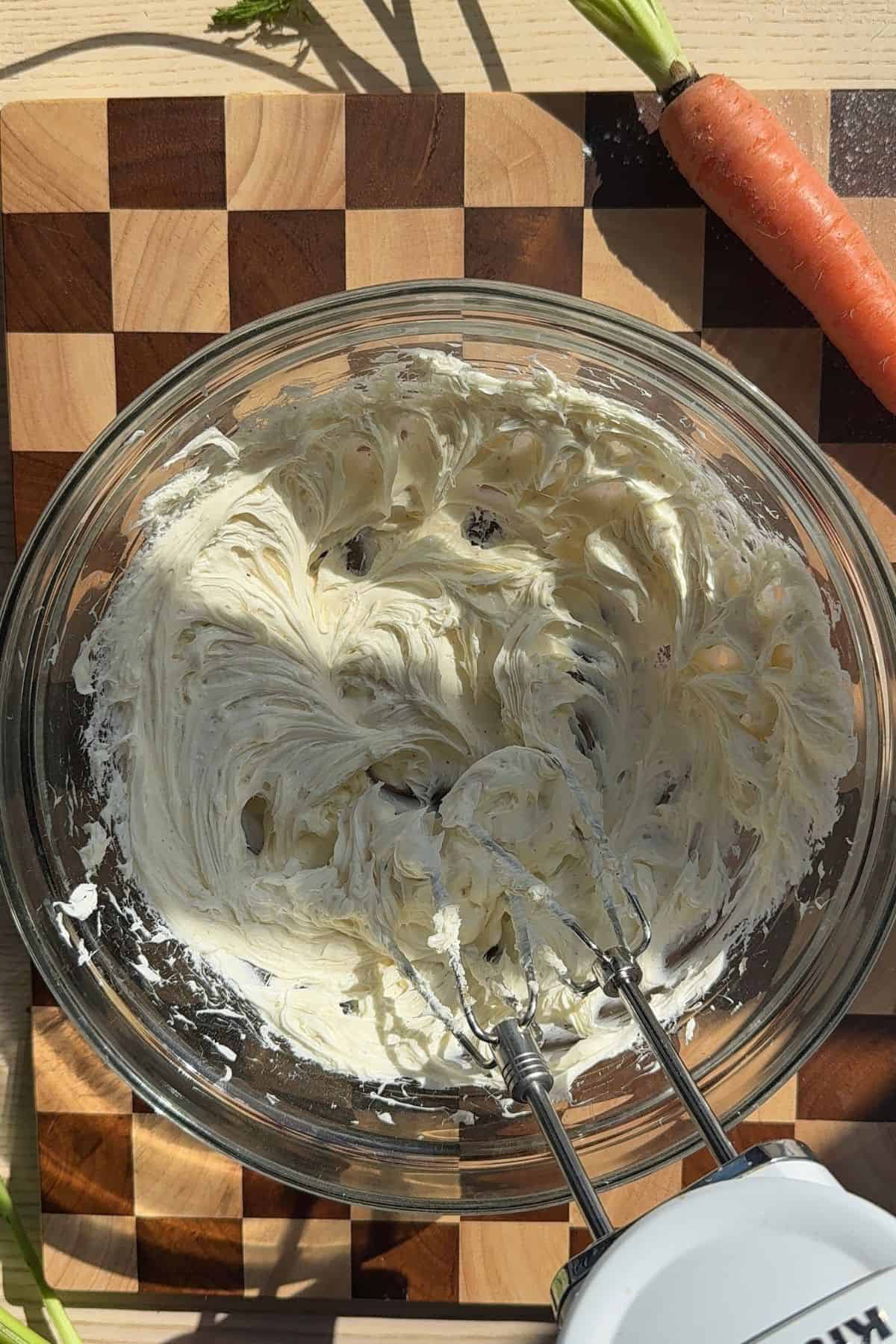 Cream cheese frosting being mixed in a bowl with a hand mixer.