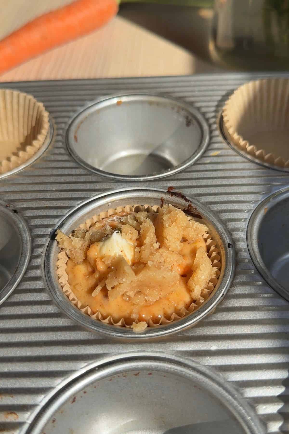 An unbaked carrot cake muffin in a muffin tin.
