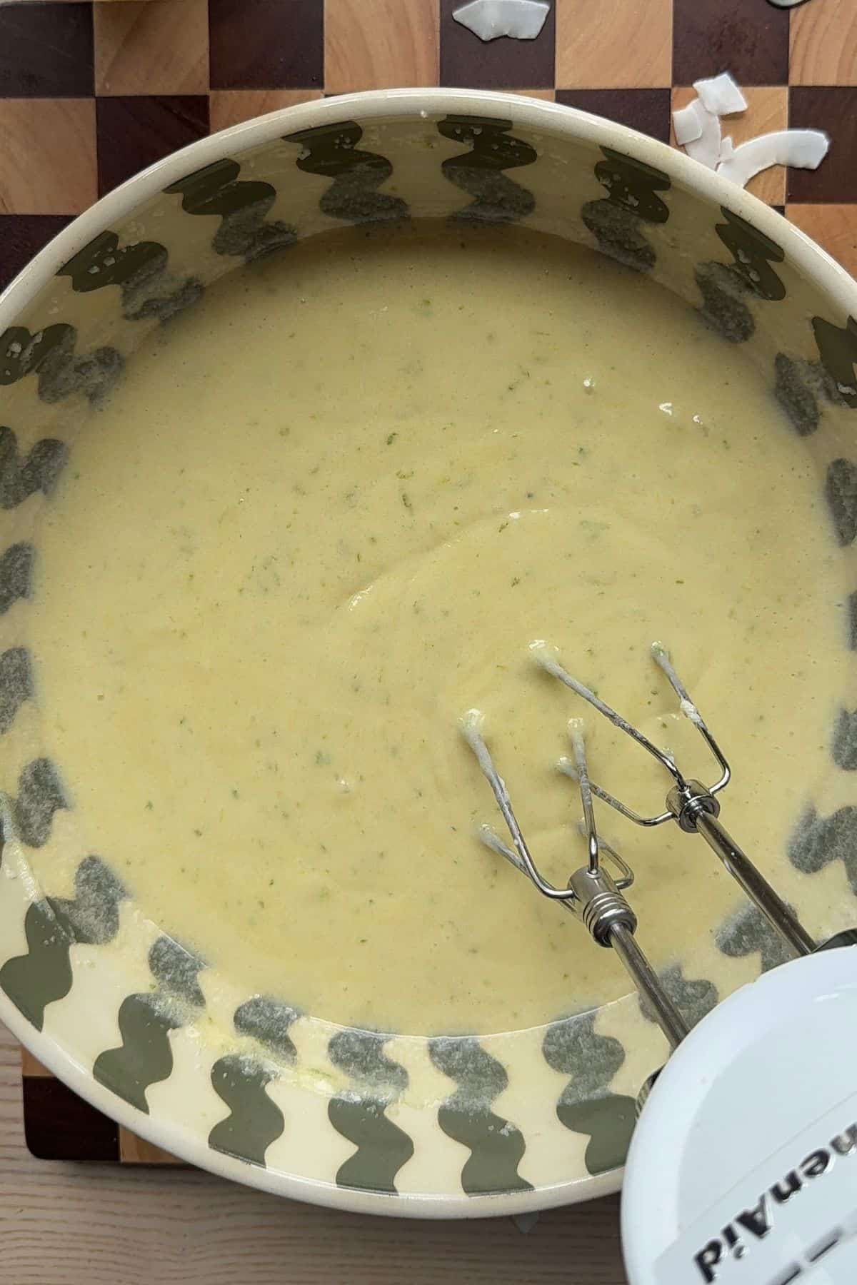 Wet ingredients for a coconut lime cake mixed together in a mixing bowl with a hand mixer.