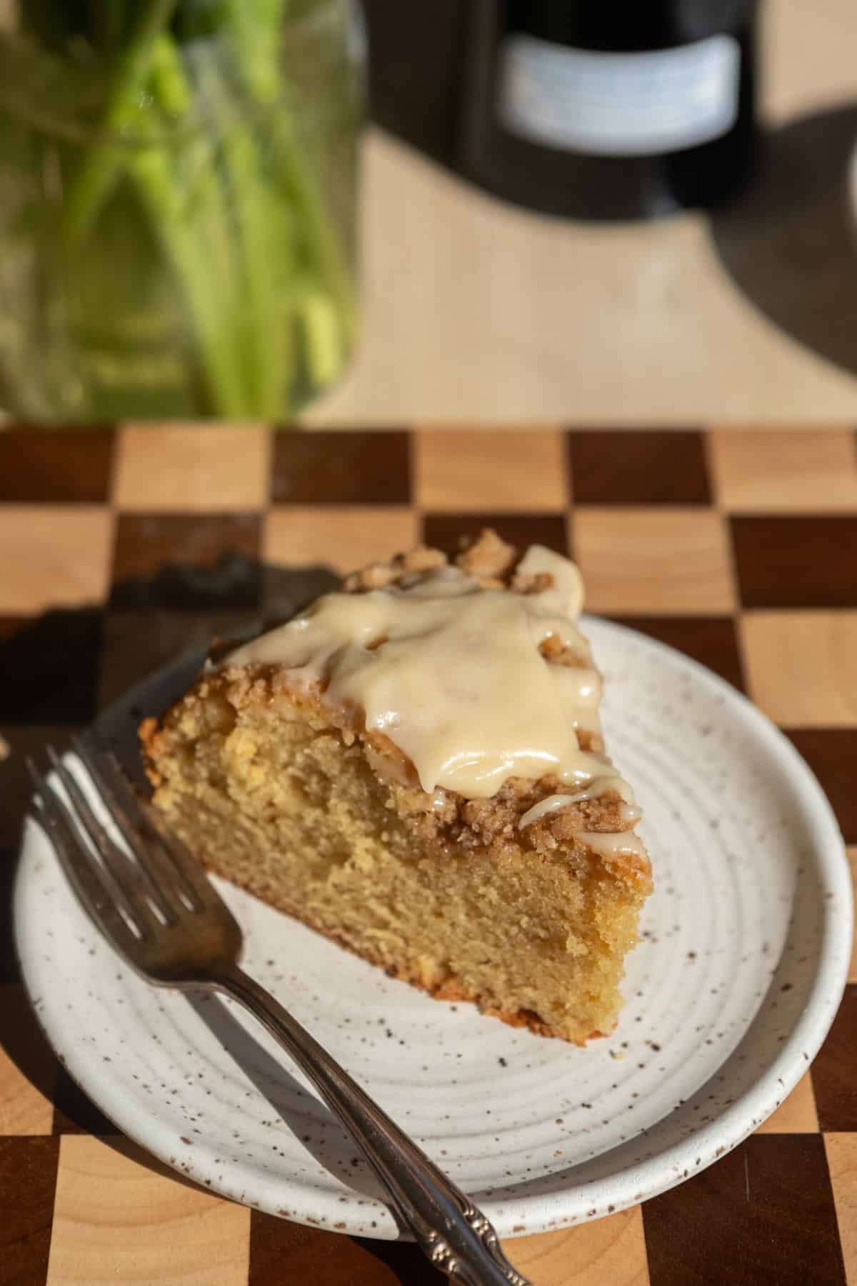 A slice of coffee cake with icing on a white plate with a fork.