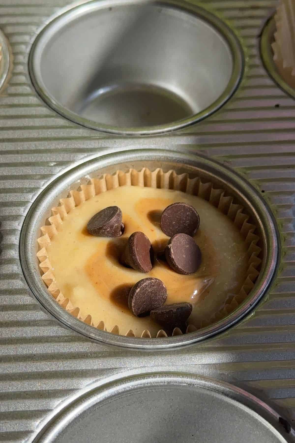 An unbaked muffin in a muffin tin topped with chocolate chips.