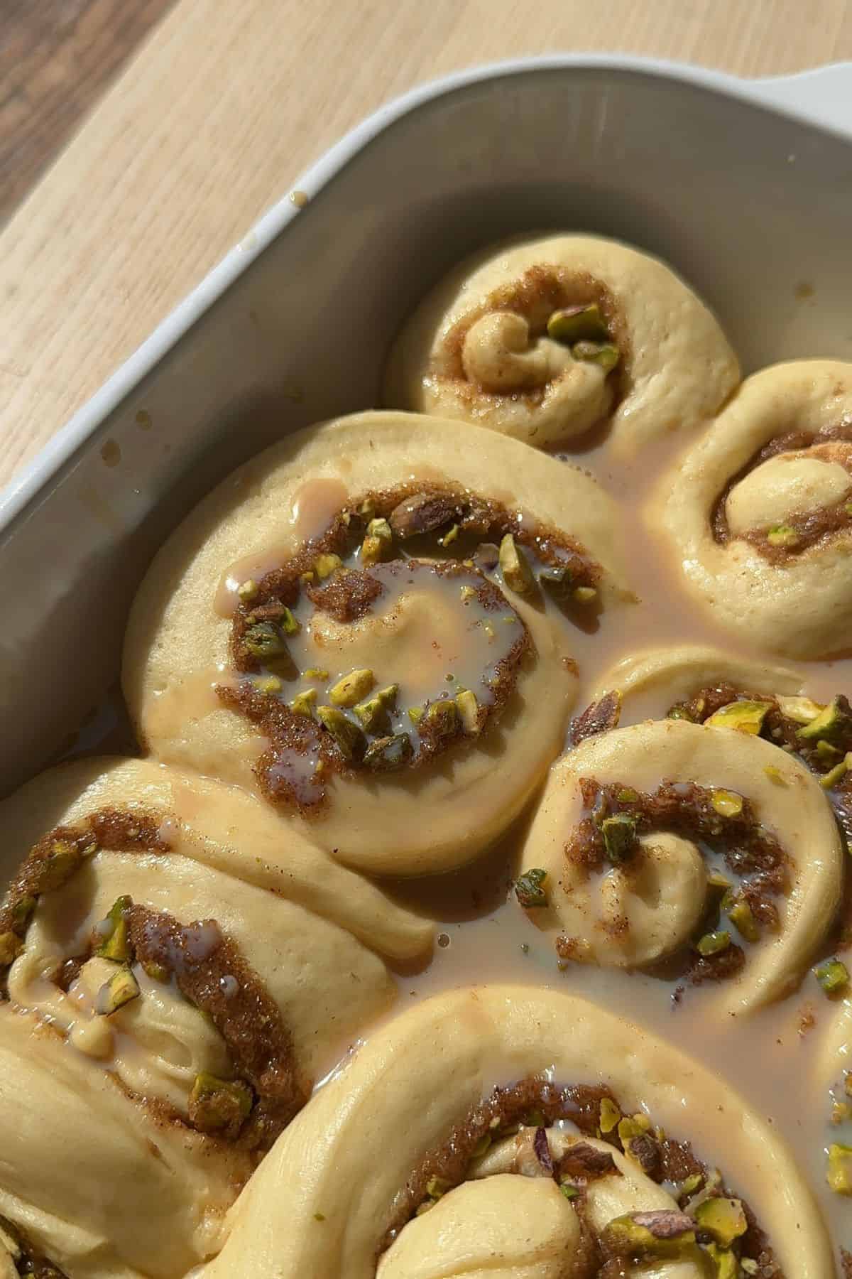 Unbaked pistachio cinnamon rolls with an Irish cream drizzle in a baking dish.