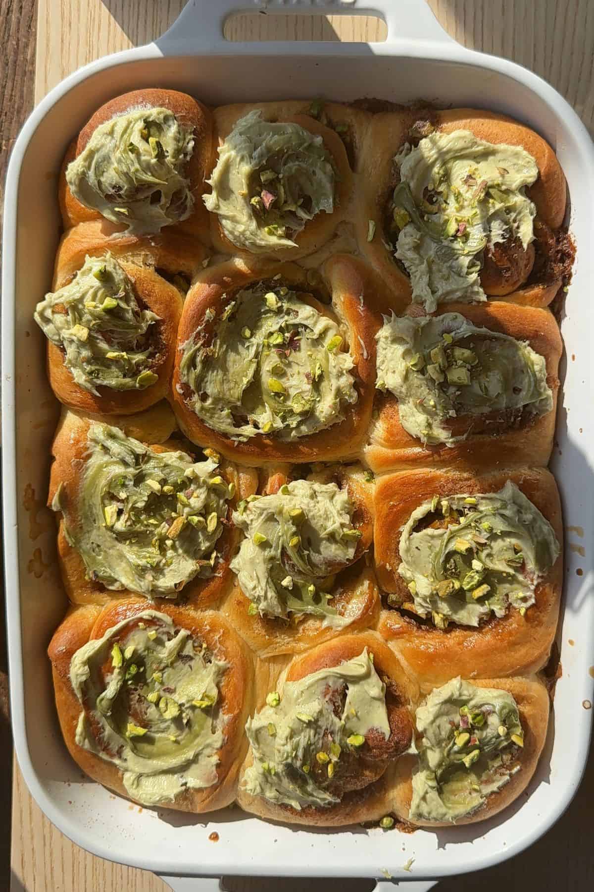 Cinnamon rolls with green frosting in a white ceramic baking dish.