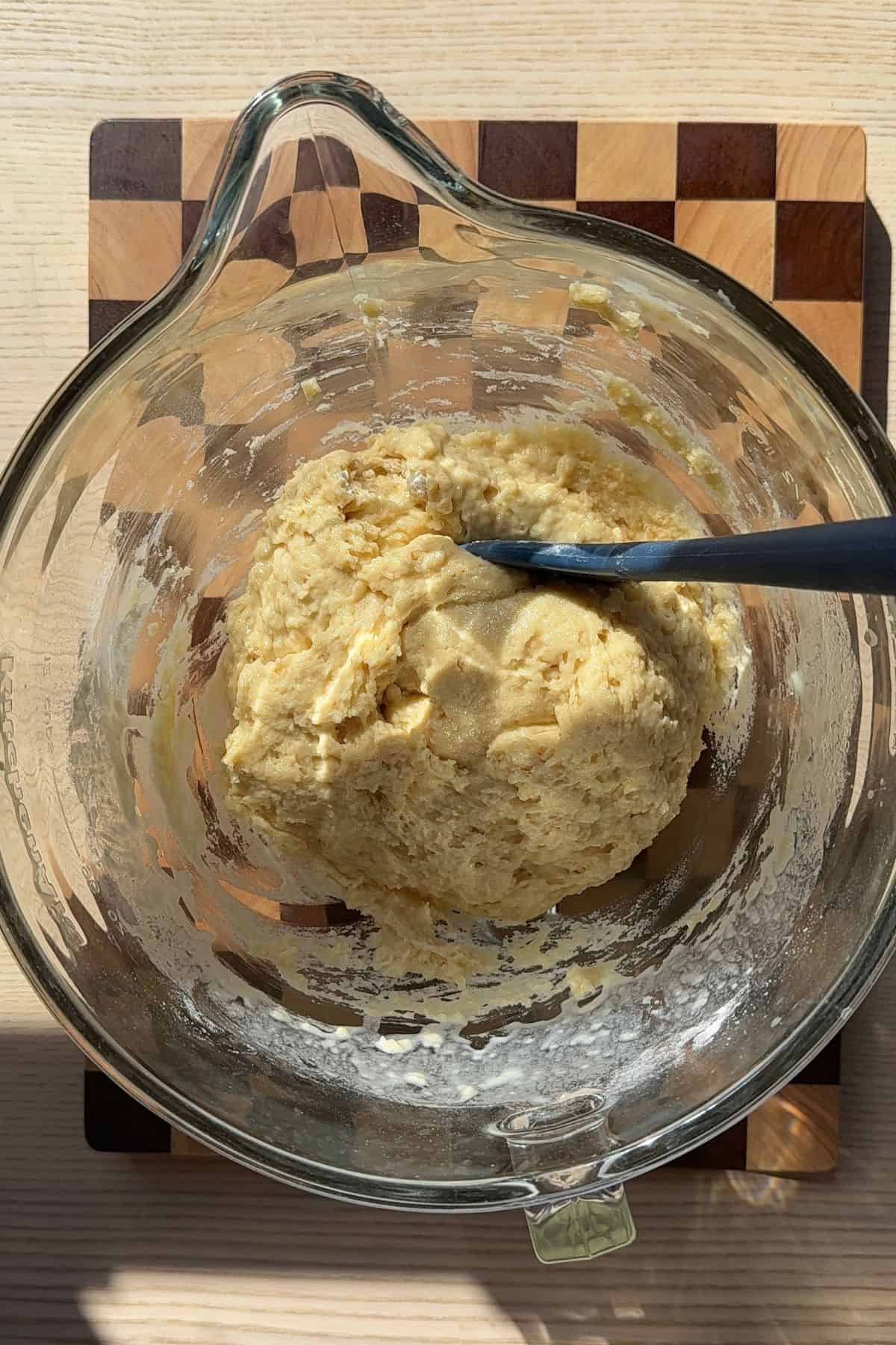 Dough in a glass bowl with a rubber spatula.