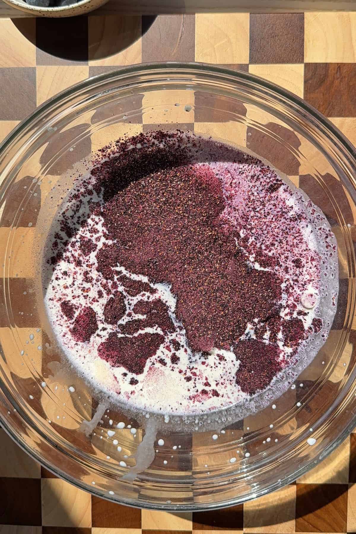 White chocolate, heavy cream, and crushed freeze-dried blueberry in a large bowl.