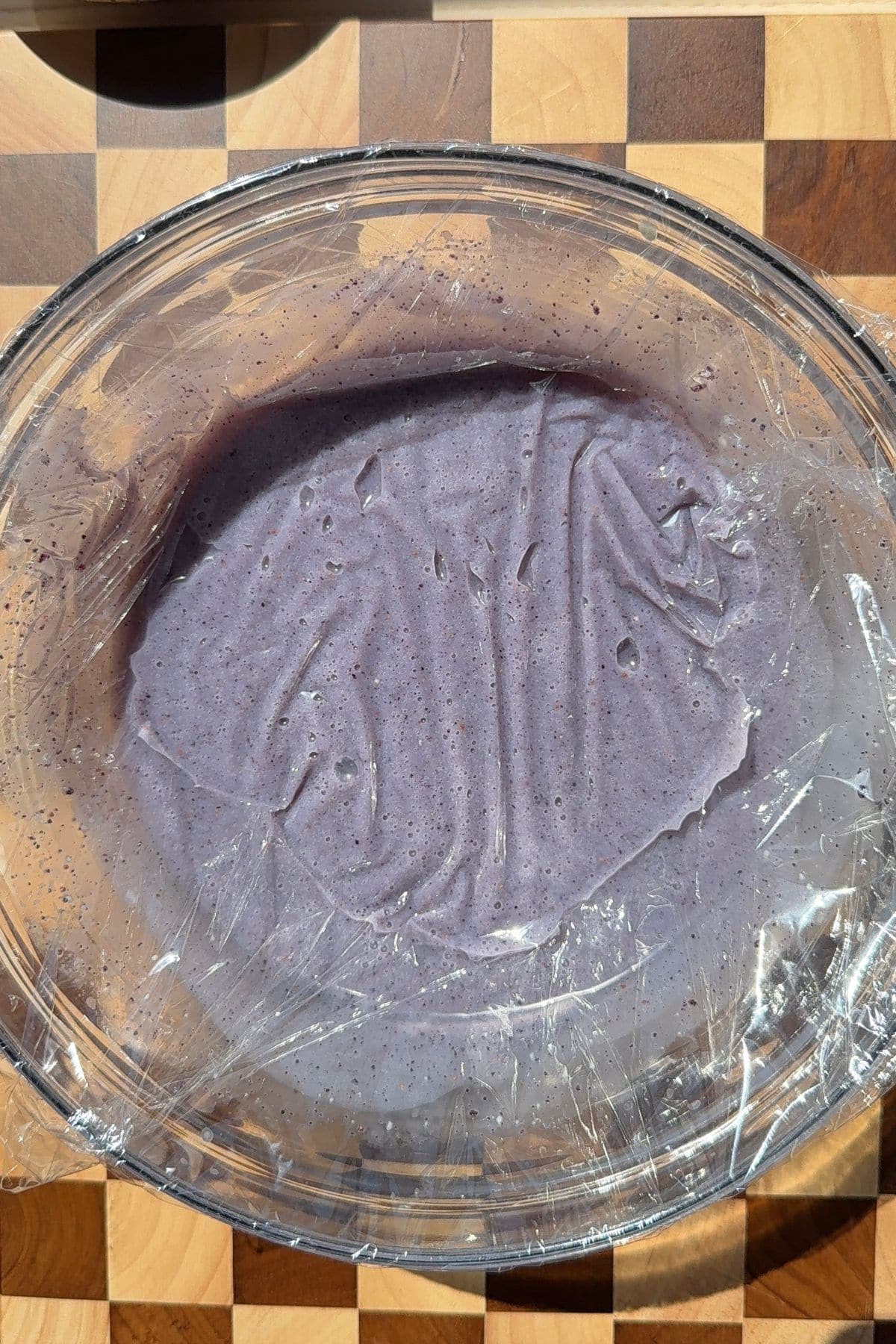 Purple ganache in a bowl covered with plastic wrap.