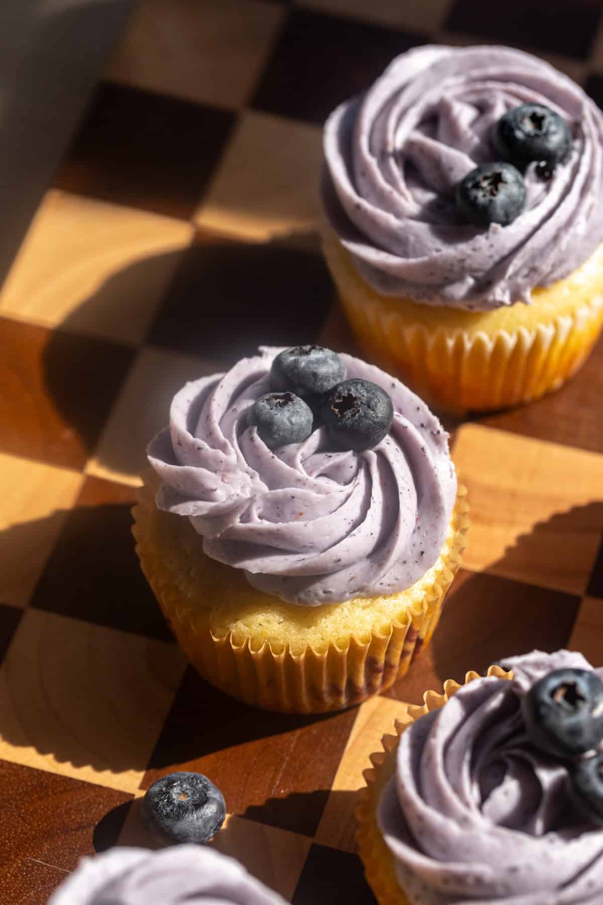 Cupcakes garnished with berries on a checkered board.