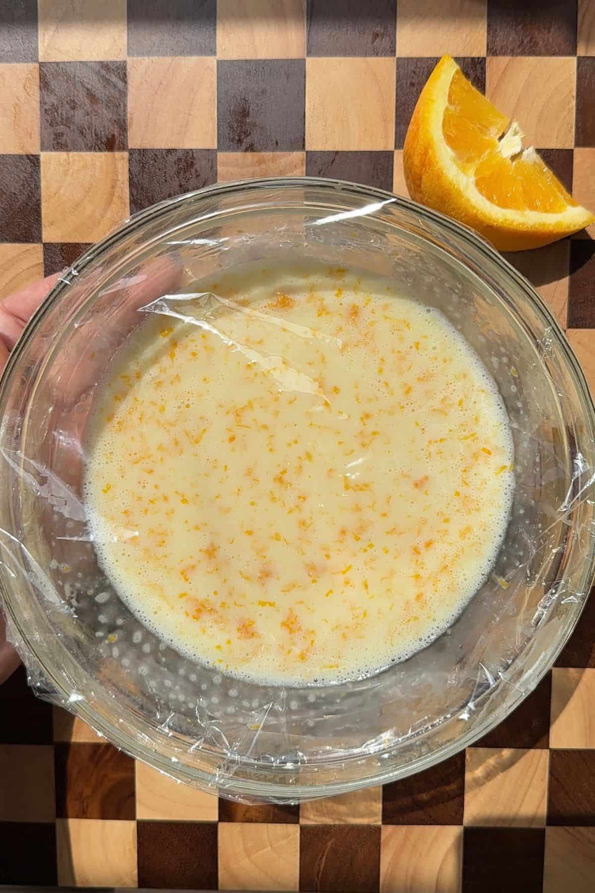 A bowl of orange ganache covered with plastic wrap.