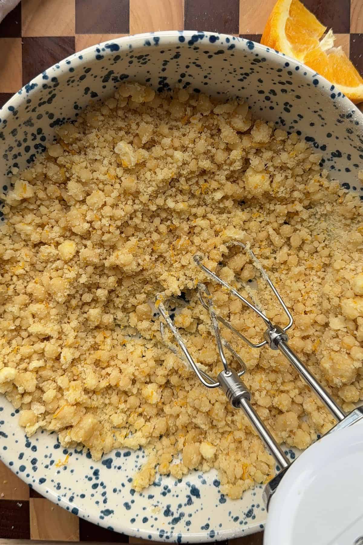 Dry ingredients coated in butter in a bowl with a hand mixer.